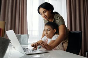Mother helping child type on laptop computer